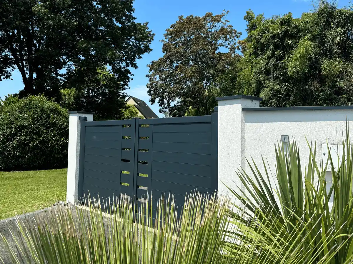 Portail alu battant installé par Pyrénées Automatismes dans un jardin avec beaucoup de végétation